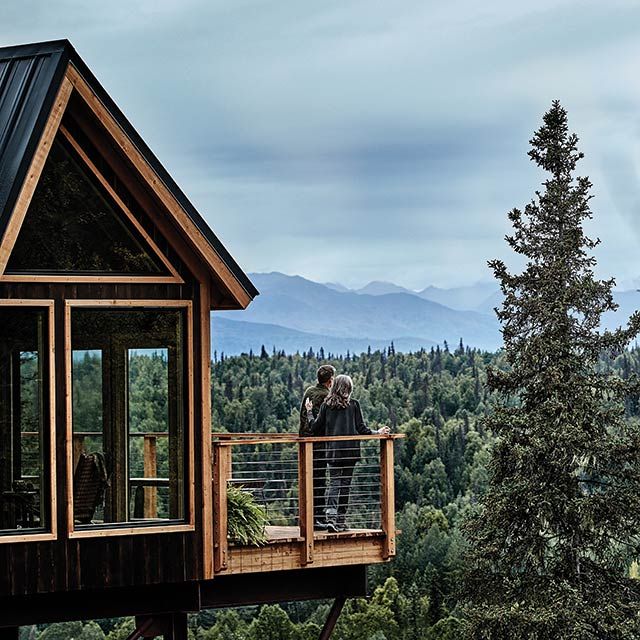 Couple standing on balcony, overlooking the forest and mountains ...